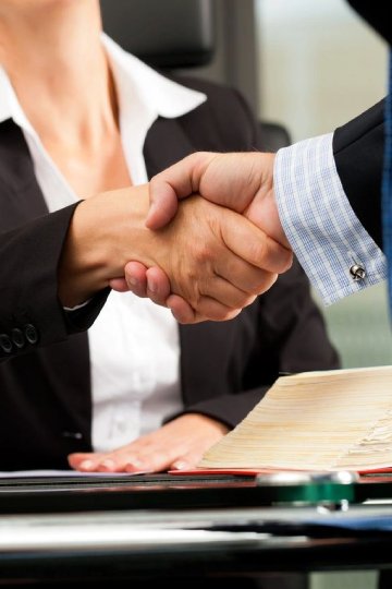 Two people shaking hands over a table.