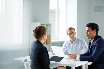 Three people sitting at a table talking to each other.