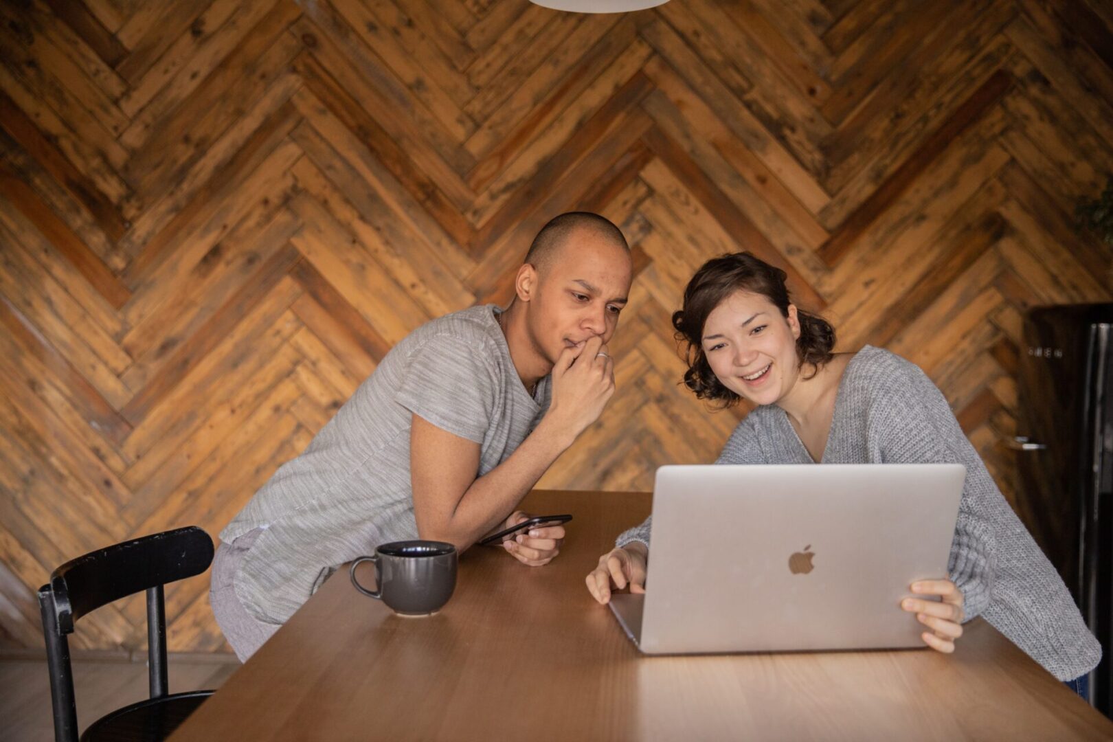 A man and woman sitting at a table looking at a laptop.